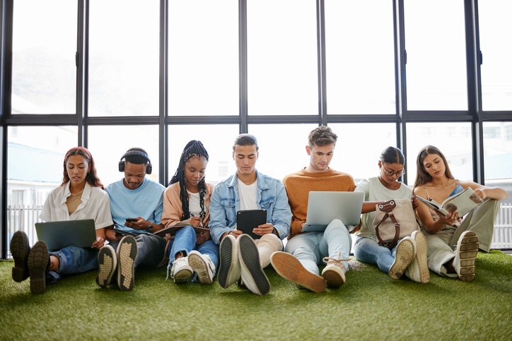 siete jovenes sentados juegan con ordenadores, teléfonos y tablet