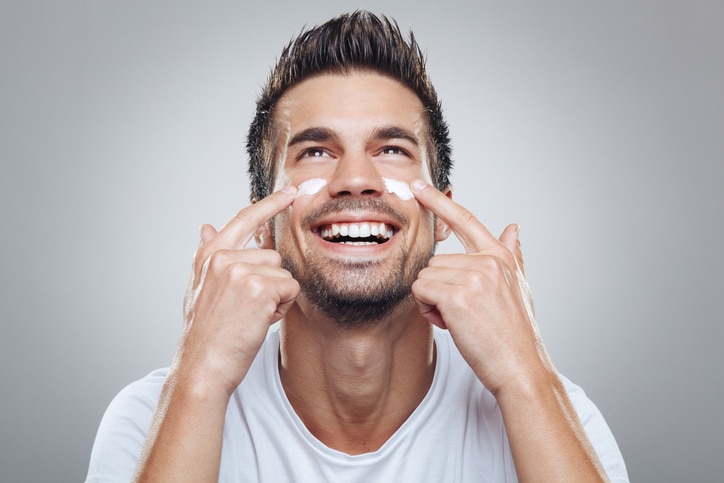 Hombre sonriente echándose crema hidratante